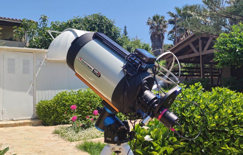 Pegasus NYX-101 harmonic mount with a Celestron EdgeHD telescope set up outdoors in a backyard under bright daylight with greenery in the background.
